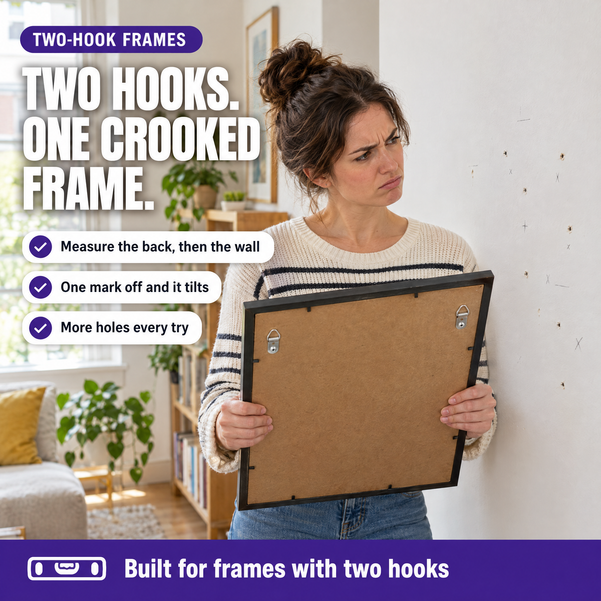 Woman holding a frame with two hooks next to a wall with extra nail holes